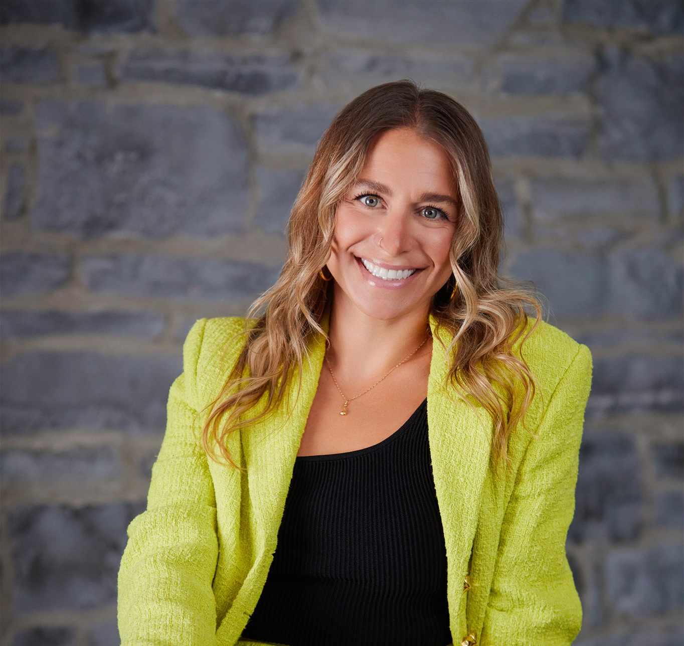 A headshot of a woman sitting down wearing a lime green pant suit
