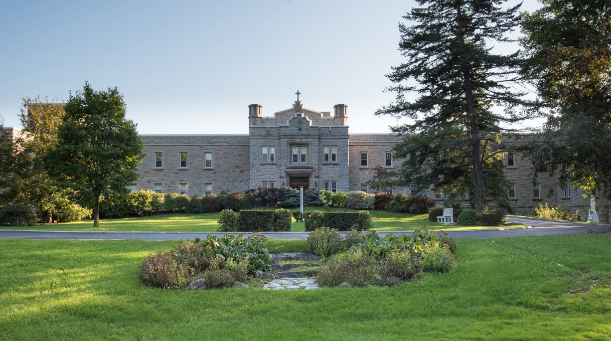An old stone building with grass and trees in front, and a blue sky in the background