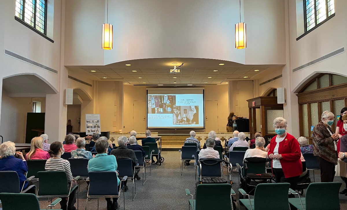An old chapel turned into an auditorium with people sitting in chairs set up in rows facing a screen at the front of the room