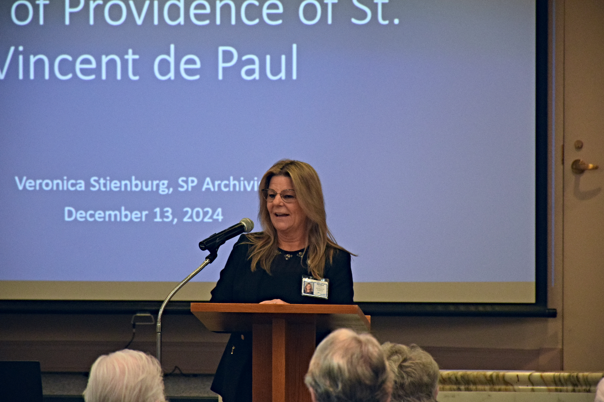 A person standing at a podium in front of a projector screen.