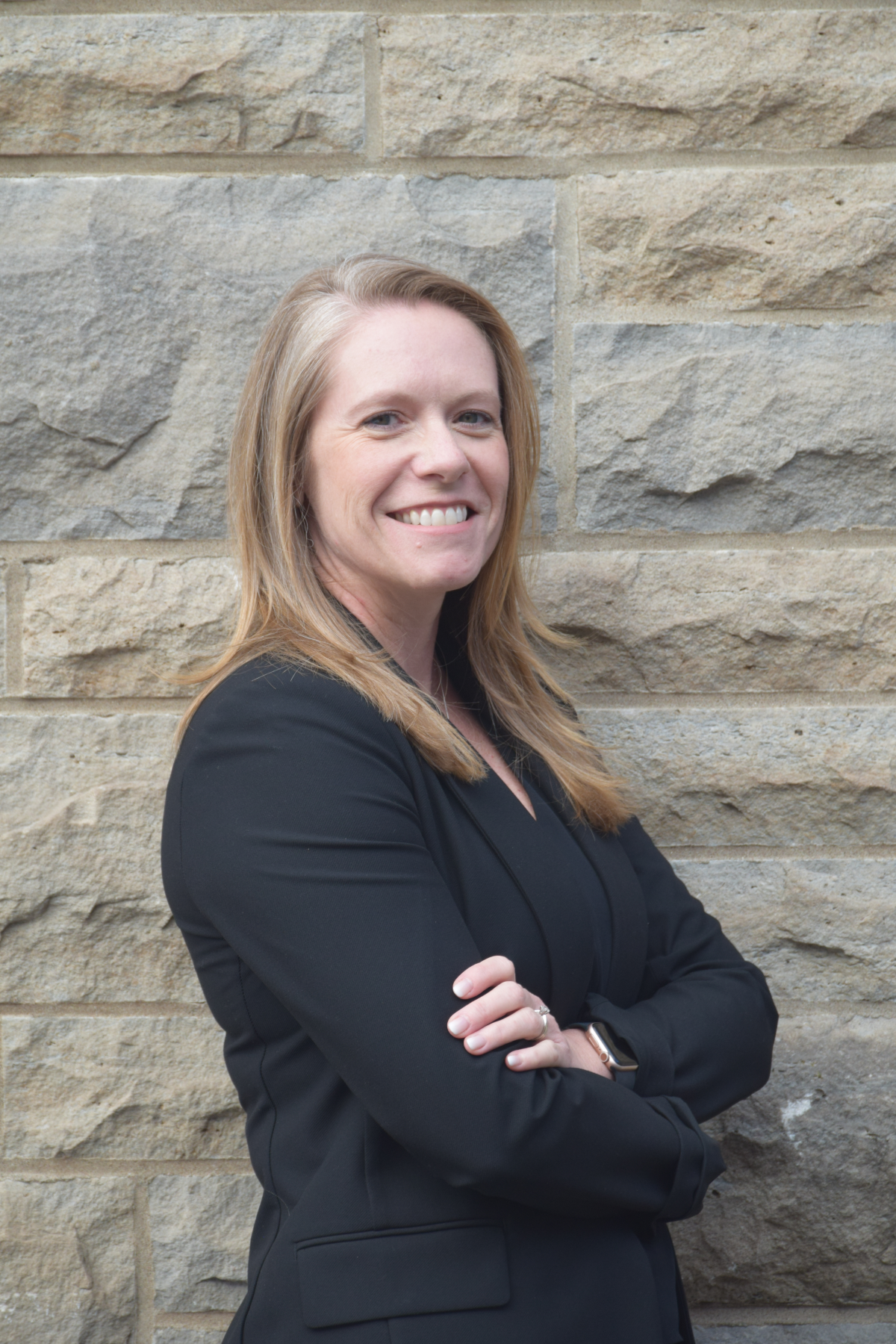 headshot of a woman wearing a black blazer standing against a limestone wall.
