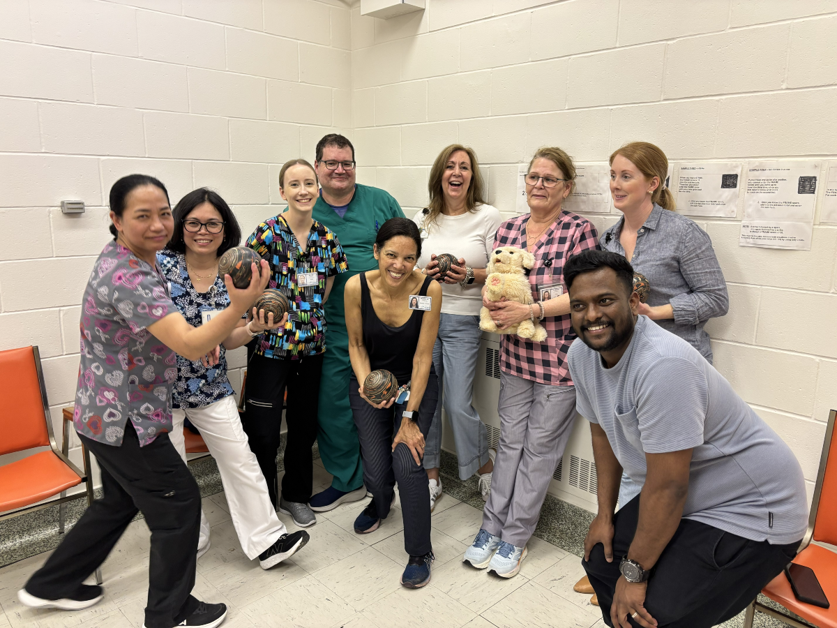 A group of 9 people huddled together for a picture, with the person in the centre holding a small bowling ball.